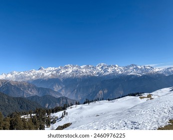 The image features a snowy mountain range with a clear sky in the background. The snow-covered terrain includes trees and a massif, creating a winter landscape.