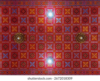 The image features a vibrant and intricately designed ceiling with a geometric pattern, adorned with red, gold, and blue colors.