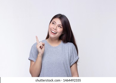 Image Of Feeling Smile And Happy. Cheerful Young Asian Woman With Brunette Long Hair In Casual Shirt Smiling With Teeth Pointing Up With Index Finger To Copy Space On White Background.