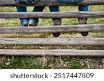 Image of the feet of a cowboy and cowgirl as they sit on an old wooden fence together. 