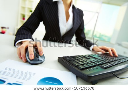 Image of female hands pushing keys of a computer mouse and keyboard with papers near by