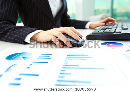 Image of female hands pushing keys of a computer mouse and keyboard with papers near by