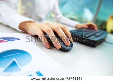 Image of female hands pushing keys of a computer mouse and keyboard with papers near by
