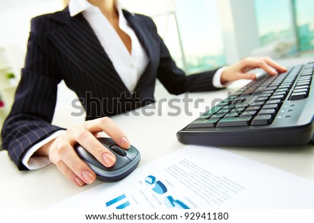 Image of female hands pushing keys of a computer mouse and keyboard with papers near by