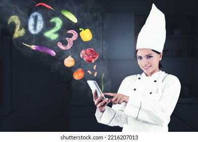 Image of female magician chef using a cellphone with flying food ingredients and smoke shaped of 2023 number in the kitchen - Shutterstock ID 2216207013