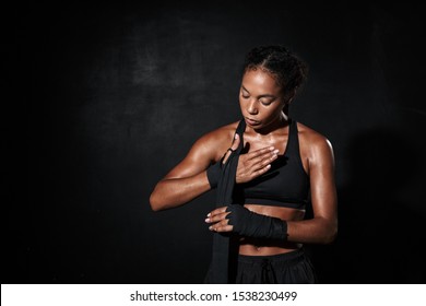 Image of feminine african american woman in sportswear wearing boxing hand wraps isolated over black background - Powered by Shutterstock