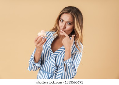 Image of feminine young woman with long hair eating tasty cupcake isolated over beige background in studio - Shutterstock ID 1533565691