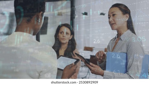 Image of financial data and graphs over diverse female cowoerkers in office. Business, finance, economy, cooperation and communication concept digitally generated image.