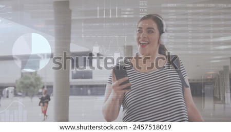 Image of financial data and graphs over caucasian woman wearing headphones using smartphone. finance, economy, communication and technology concept digitally generated image.