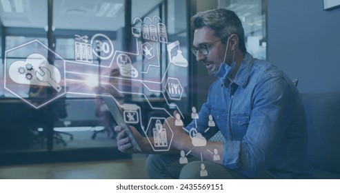 Image of financial data processing over businessman with face mask using tablet in office. global business and digital interface during covid 19 pandemic concept digitally generated image.