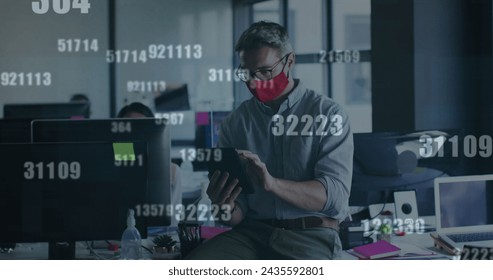 Image of financial data processing over businessman with face mask using tablet in office. global business and digital interface during covid 19 pandemic concept digitally generated image.