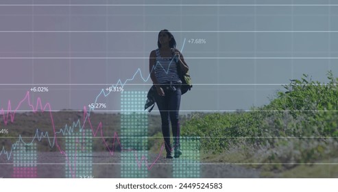 Image of financial data processing over biracial woman walking on street. Global business, finances and digital interface concept digitally generated image.