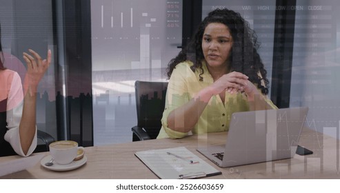 Image of financial data processing over diverse businesswomen in office. Global business, finance, computing and data processing concept digitally generated image.