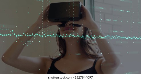 Image of financial data processing over caucasian woman using vr headset. Global technology, finances and digital interface concept digitally generated image.