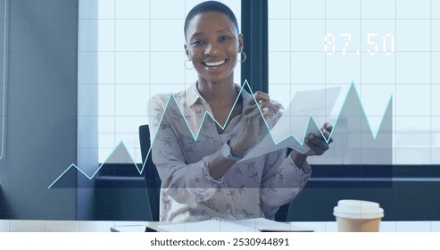 Image of financial data processing over african american businesswoman working in office. Global business, finance, computing and data processing concept digitally generated image.