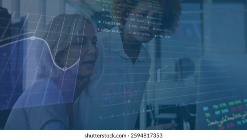 Image of financial data processing over diverse colleagues using laptop in office. Global business, computing, communication and digital interface concept digitally generated image.