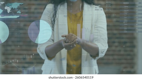 Image of financial data processing over businesswoman disinfecting hands. global business, data processing and digital interface during covid 19 pandemic concept digitally generated image.