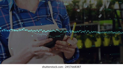 Image of financial graphs over caucasian woman with payment terminal. Finance, economy, business and wireless payments concept digitally generated image.