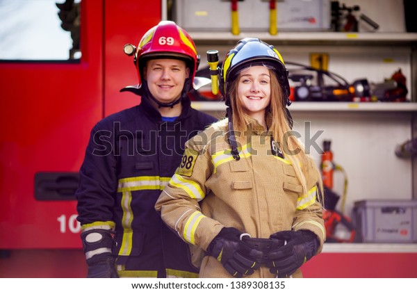 Image of firefighters women and men in helmets\
looking at camera near fire\
truck