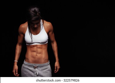 Image of fitness woman in sports clothing looking down. Young female model with muscular body. Horizontal studio shot with copy space on black background.