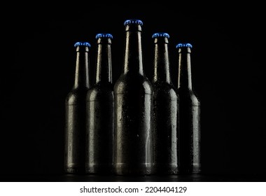 Imagen de cinco botellas de cerveza con tapones de corona azules, con espacio para copiar sobre fondo negro. El concepto de alcohol para beber, refresco y celebración del día mayor.