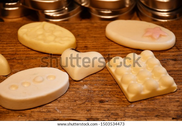 An image of five different decorative soap bars of various shapes of white, light yellow and light pink colors made of natural ingredients lying on a wooden surface