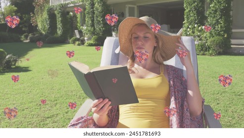 Image of floral hearts falling over cauacsian woman in sun lounger reading book in garden. relaxation, happiness and wellbeing concept digitally generated image. - Powered by Shutterstock