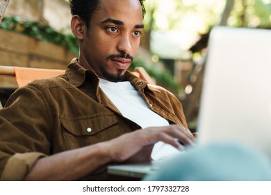 Image of focused african american couple working with laptop while sitting in cafe outdoors - Powered by Shutterstock