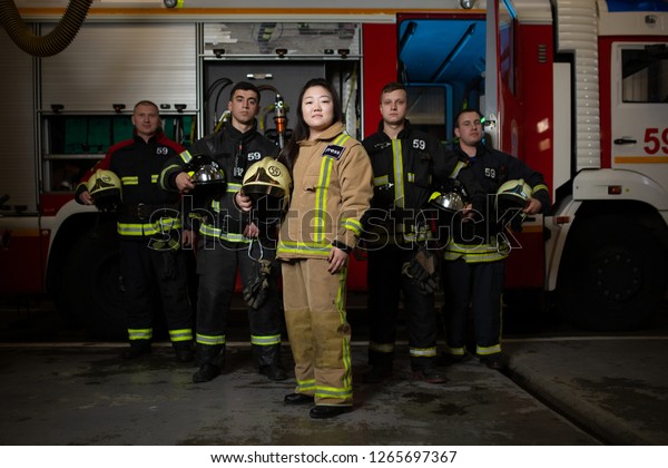 Image of four male and female firefighters on\
background of fire truck