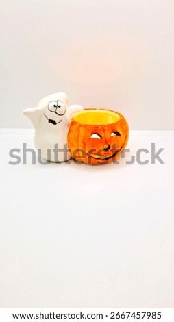 Image of a friendly ghost and bright orange jack-o-lantern votive holder with a candle inside to decorate a space for Halloween. Halloween white ghost orange pumpkin decoration with warm candle flame.