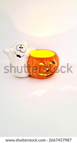 Image of a friendly ghost and bright orange jack-o-lantern votive holder with a candle inside to decorate a space for Halloween. Halloween white ghost orange pumpkin decoration with warm candle flame.