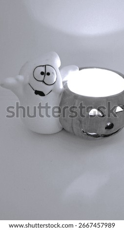 Image of a friendly ghost and bright orange jack-o-lantern votive holder with a candle inside to decorate a space for Halloween. Halloween white ghost orange pumpkin decoration with warm candle flame.