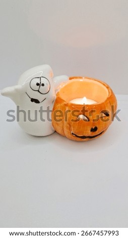 Image of a friendly ghost and bright orange jack-o-lantern votive holder with a candle inside to decorate a space for Halloween. Halloween white ghost orange pumpkin decoration with warm candle flame.