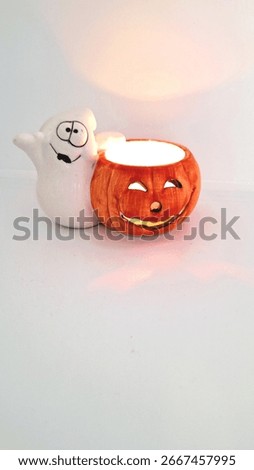 Image of a friendly ghost and bright orange jack-o-lantern votive holder with a candle inside to decorate a space for Halloween. Halloween white ghost orange pumpkin decoration with warm candle flame.