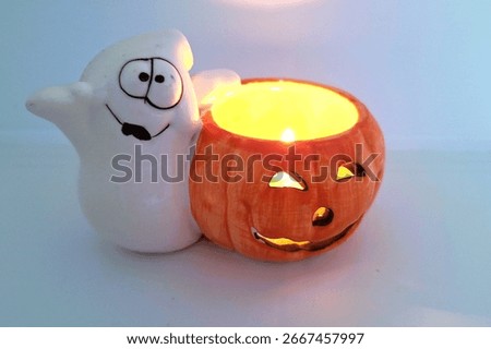 Image of a friendly ghost and bright orange jack-o-lantern votive holder with a candle inside to decorate a space for Halloween. Halloween white ghost orange pumpkin decoration with warm candle flame.