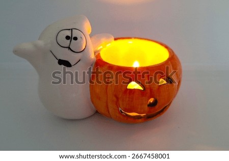 Image of a friendly ghost and bright orange jack-o-lantern votive holder with a candle inside to decorate a space for Halloween. Halloween white ghost orange pumpkin decoration with warm candle flame.