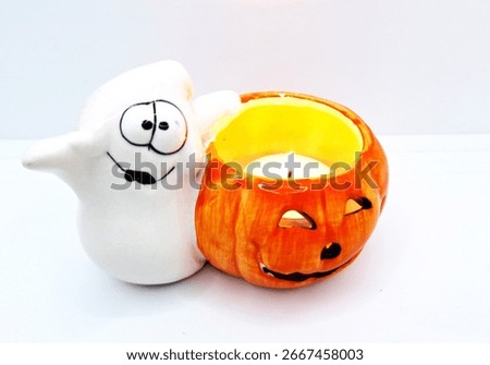 Image of a friendly ghost and bright orange jack-o-lantern votive holder with a candle inside to decorate a space for Halloween. Halloween white ghost orange pumpkin decoration with warm candle flame.