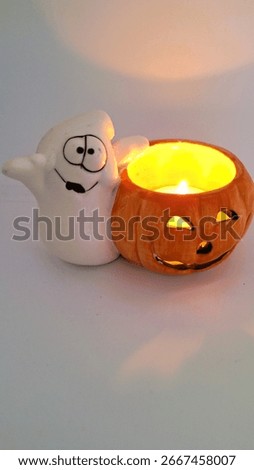 Image of a friendly ghost and bright orange jack-o-lantern votive holder with a candle inside to decorate a space for Halloween. Halloween white ghost orange pumpkin decoration with warm candle flame.