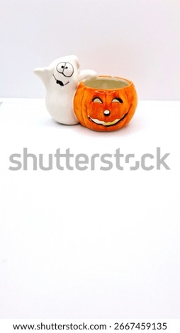 Image of a friendly ghost and bright orange jack-o-lantern votive holder with a candle inside to decorate a space for Halloween. Halloween cartoonish ghost, orange pumpkin decoration with unlit candle