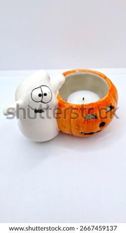 Image of a friendly ghost and bright orange jack-o-lantern votive holder with a candle inside to decorate a space for Halloween. Halloween cartoonish ghost, orange pumpkin decoration with unlit candle