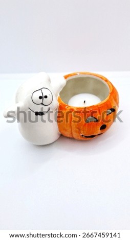 Image of a friendly ghost and bright orange jack-o-lantern votive holder with a candle inside to decorate a space for Halloween. Halloween cartoonish ghost, orange pumpkin decoration with unlit candle