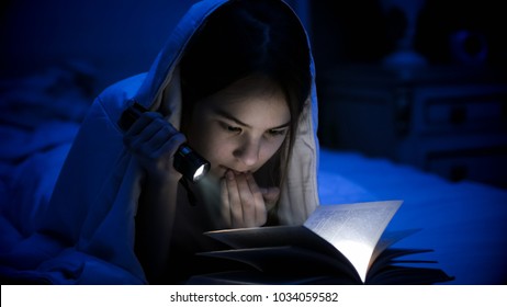 Image of girl with flashlight reading scary book under blanket