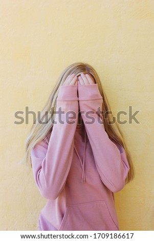 An image of a girl hiding her face behind her hands. 