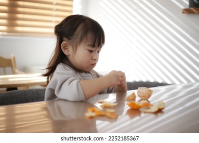 Image of a girl peeling and eating a mandarin orange - Shutterstock ID 2252185367