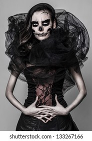 Image of a girl who is posing with a skull mask make up on the grey background