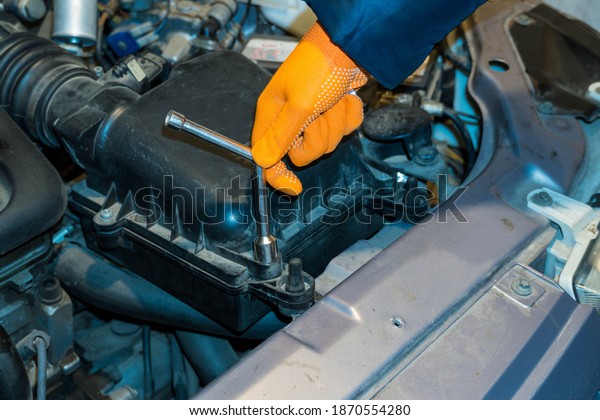 Image of a\
gloved hand holding a wrench while unscrewing the car\'s air filter.\
Auto repair and maintenance\
concept.
