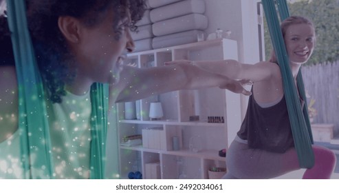 Image of glowing green particles over happy diverse teenage girls practicing aerial yoga. Yoga, wellbeing, energy, healthy lifestyle, connection and communication, digitally generated image. - Powered by Shutterstock