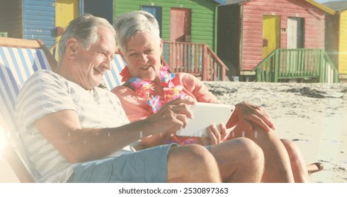 Image of glowing light over portrait of happy senior couple using tablet in deckchairs on beach. retirement and senior life concept digitally generated image. - Powered by Shutterstock