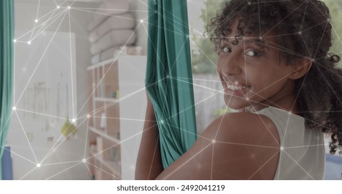 Image of glowing network over happy biracial teenage girl practicing aerial yoga. Wellbeing, energy, fitness, connection and healthy lifestyle, digitally generated image. - Powered by Shutterstock