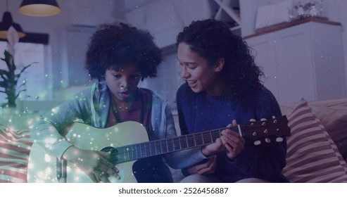 Image of glowing spots over happy biracial mother with son playing guitar. mother day and motherhood concept digitally generated image. - Powered by Shutterstock